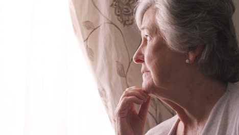 Thoughtful-senior-woman-looking-through-window