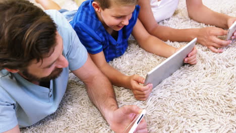 Glückliche-Familie-Mit-Tablet-Und-Smartphone-Auf-Einem-Teppich-Liegend