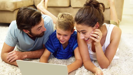 Familia-Feliz-Mirando-Una-Computadora-Portátil-Tirada-En-Una-Alfombra