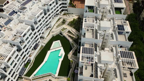 White-apartment-buildings-with-private-pool-area-in-Estepona-city,-aerial-ascend-view
