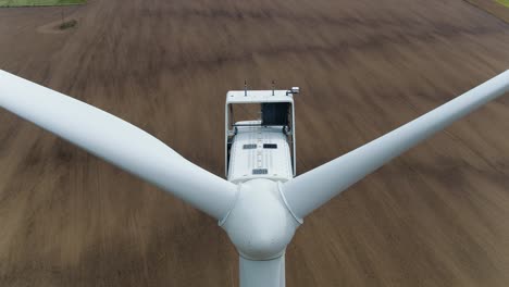 Wind-Turbine-Aerial-Drone-Shot-Ascending-Over-Propellers-with-Farmland-Background