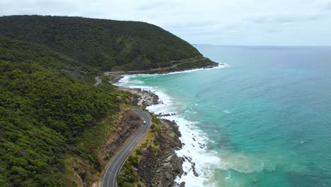 4K-Video-Eines-Einsamen-Wohnmobils,-Das-Entlang-Der-Wunderschönen-Great-Ocean-Road-Fährt,-Mit-Der-Grünen,-üppigen-Natur-Auf-Der-Einen-Straßenseite-Und-Den-Blauen-Meereswellen,-Die-Auf-Der-Anderen-Seite-Brechen.