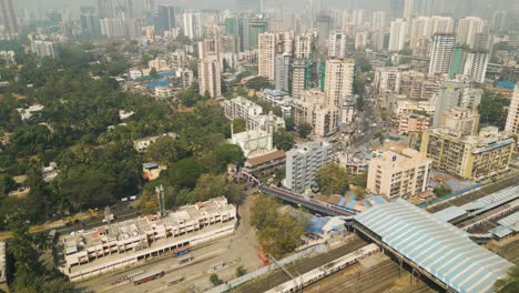 Aerial-establishing-shot-of-the-Mumbai-Skyline-with-the-train-station-beside,-India