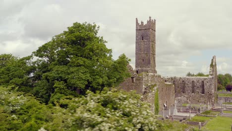 Claregalway-Friary-revealed-behind-lush-green-foliage-with-cemetery-and-tombstones