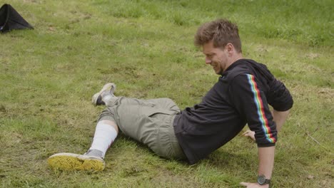 Young-man-with-a-serious-leg-injury-lying-in-the-grass,-he-tries-to-support-his-bleeding-leg-and-lays-down-in-agony
