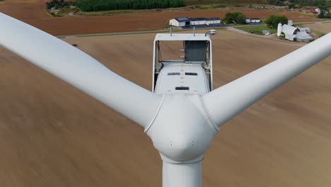 Primer-Plano-De-Una-Turbina-Eólica-Con-Un-Dron-Aéreo-Ascendiendo-Sobre-Un-Campo-De-Trigo-En-El-Fondo