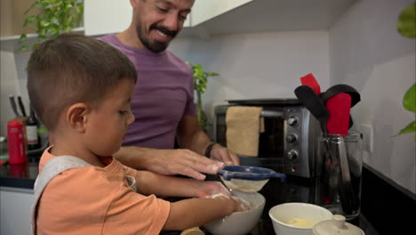Slow-motion-of-a-young-mexican-latin-boy-sifting-sieving-flour-at-the-kitchen-having-fun-with-his-dad-smiling-and-looking-at-the-camera