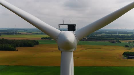 Propellerblätter-Einer-Windturbine-Mit-Einer-Luftaufnahme,-Die-über-Ihnen-Aufsteigt,-Und-Ackerland-Im-Hintergrund