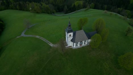 Standing-in-middle-of-lush-green-meadow,-Slovenian-church,-aerial-dolly