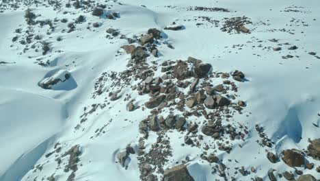 Snow,-white,-blanket-like-cover-over-mountain-rocks,-aerial-reveal