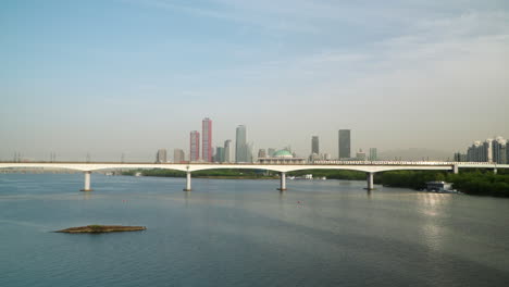 Die-U-Bahn-Fährt-Auf-Der-Dangsan-Eisenbahnbrücke-über-Den-Han-Fluss-In-Seoul-Mit-Dem-Stadtteil-Yeongdeungpo-Im-Hintergrund,-Das-Licht-Der-Untergehenden-Sonne-Spiegelt-Sich-Im-Fahrenden-Zug