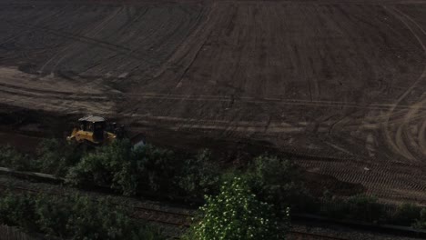 Aerial-view-tracking-bulldozer-working-new-housing-estate-land-beside-sunlit-morning-railway-tracks