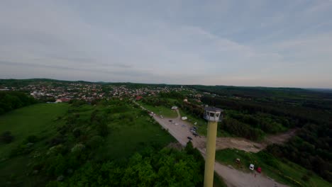 Tall-watchtower-near-town-and-forest-landscape,-aerial-FPV-orbit-view