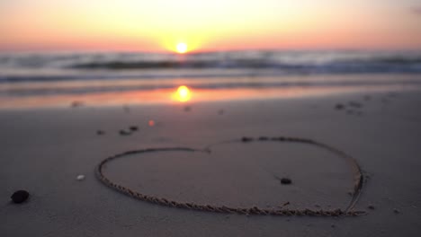 Heart-symbol-drawn-on-sand-against-a-backdrop-of-sunset-over-the-sea