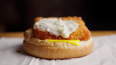 Raised-bun-reveals-mayo-on-fried-fish-burger-with-mayonnaise-and-cheese