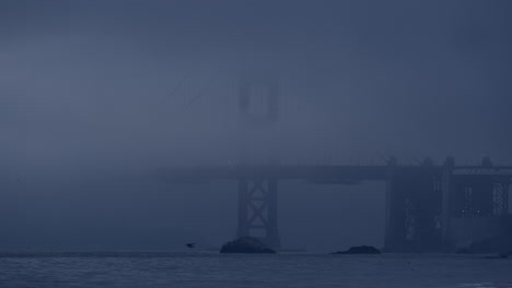 Golden-Gate-Bridge-shrouded-in-fog-with-waves-gently-crashing-in-San-Francisco-Bay,-viewed-from-Baker-Beach