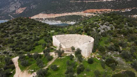 Fly-Up-Above-1st-Century-BCE-Ancient-Amphitheater-Overlooking-the-Mediterranean-Sea-Towards-Greek-Islands,-Antiphellos-Theatre-with-Coastal-View,-in-Kas,-Turkey:-Turkish-South-Coast