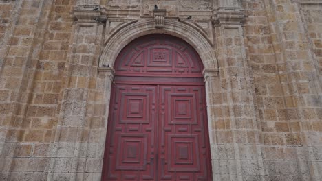 Las-Palomas-Se-Reúnen-Cerca-De-Las-Grandes-Puertas-Rojas-De-La-Iglesia-De-San-Pedro-Claver-En-Cartagena,-Colombia.