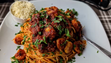 Ein-Teller-Gefüllt-Mit-Spaghetti-Und-Meeresfrüchten-In-Tomatensauce,-Geriebenem-Käse-An-Der-Seite