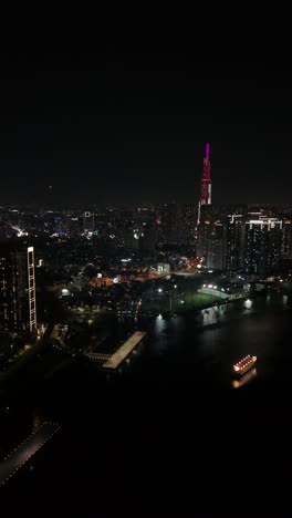 Stunning-nighttime-aerial-view-of-Ho-Chi-Minh-City,-Vietnam-Saigon-with-city-lights-and-waterfront,-vertical-video