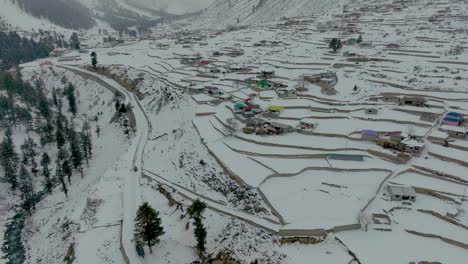 Drone-footage-flying-over-village-and-colourful-houses-over-the-valley-of-Naltar-in-Gilgit-Pakistan-in-winter-covered-in-snow