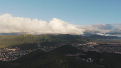 High-drone-pan-of-Salta-City,-nestled-in-between-mountains,-dramatic-clouds
