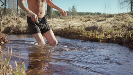 Man-wearing-booties-enter-country-stream-for-therapeutic-cold-plunge,-slomo