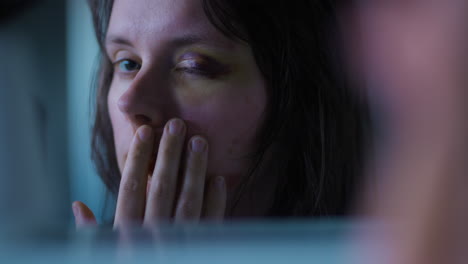 Close-up-shot-of-a-young-and-scared-Woman-looking-at-her-injured-and-bruised-eye-in-the-mirror-with-horror-in-her-eyes-in-slow-motion