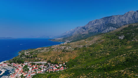 Drone-flying-over-a-town-on-the-coastline-of-the-Makarska-riviera,-summer-in-Croatia