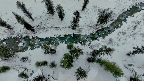 Imágenes-De-Drones-Vista-De-Arriba-Hacia-Abajo-Descendiendo-Sobre-El-Lago-Con-Agua-Azul-Limpia-Mientras-Nieva-Y-Una-Montaña-Cubierta-De-Nieve