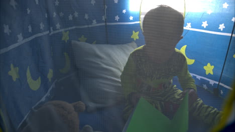 Slow-motion-of-a-young-mexican-latin-boy-in-pajamas-sitting-inside-his-blue-castle-tent-reading-a-book-alone