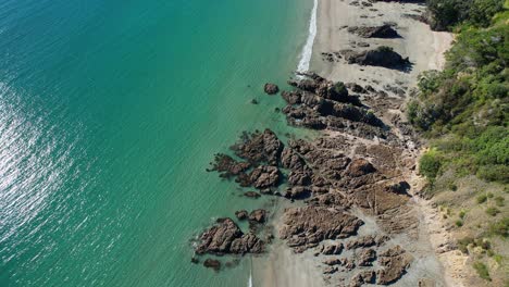 Rocky-Little-Oneroa-Beach-With-Tranquil-Blue-Waters-On-A-Sunny-Summer-Day-In-Auckland,-New-Zealand