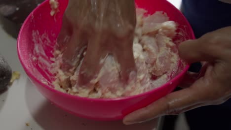 Hand-mixing-chicken-tenders-with-batter-in-a-bright-red-bowl-in-a-kitchen-setting