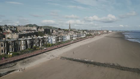 Portobello-seaside-town-in-Edinburgh-on-beautiful-sunny-morning-by-the-beach-showing-residential-buildings,-a-church-tower-and-Arthur's-Seat-in-the-background