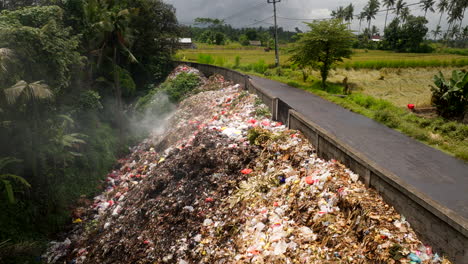 Burning-human-trash-heap-next-to-country-road-in-Bali,-Indonesia