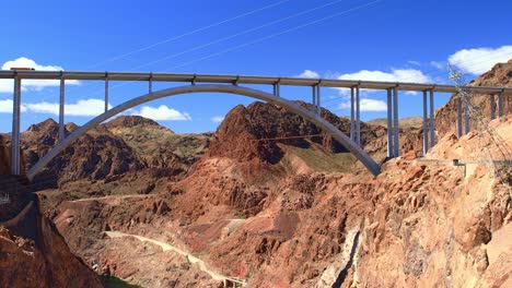 Puente-De-Carretera-Arqueado-De-La-Presa-Hoover-Con-Camión-Rojo-Cruzando-Contra-Un-Cielo-Azul-En-Nevada,-EE.UU.