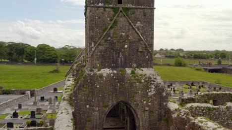Aerial-orbit-around-old-weathered-mossy-tower-of-Claregalway-Friary-as-birds-fly-around