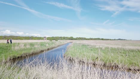 Couple-walk-along-Westwood-Marsh-fens,-scenic-peaceful-nature-trail-Suffolk