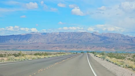 Driving-Along-Lakeshore-Road-with-Scenic-Views-of-Lake-Mead-Surrounded-by-Mountains-in-Nevada,-POV-Driving-View,-USA