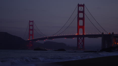 Stunning-sunrise-over-Golden-Gate-Bridge-with-ocean-waves-and-clouds-from-Baker-Beach,-San-Francisco