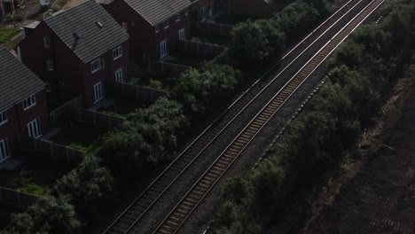 Aerial-view-overlooking-sunlit-railway-tracks-between-construction-site-new-build-housing-estate-early-morning