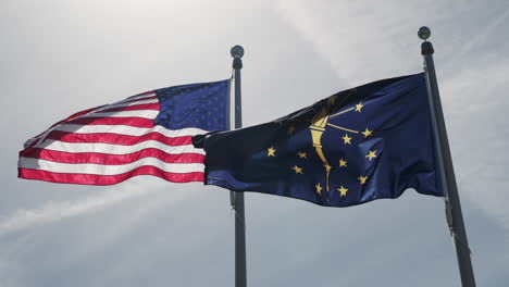 The-American-and-Indiana-flags-flutter-proudly-side-by-side,-their-vibrant-colors-contrasting-against-a-partly-cloudy-sky