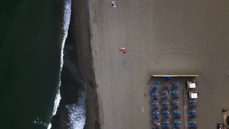 Olas-Espumosas-Del-Océano-Que-Fluyen-Sobre-Una-Playa-De-Arena-Con-Tumbonas,-Vista-Aérea-De-Arriba-Hacia-Abajo