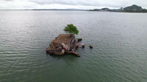 Drone-shot-of-people-fishing-of-a-small-abandoned-house-in-the-middle-of-the-ocean