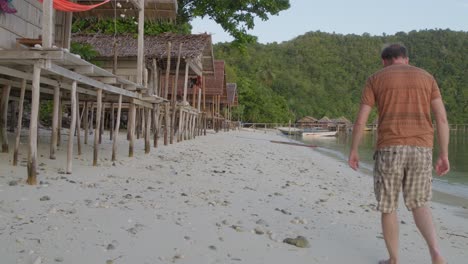 A-man-walks-along-the-sandy-beach-of-Kri-Island-in-the-Raja-Ampat-archipelago,-Indonesia