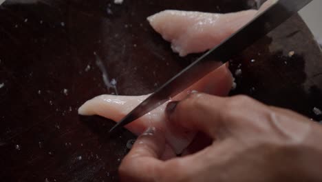 A-person-slicing-raw-chicken-breast-on-a-wooden-cutting-board,-close-up