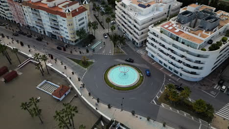 Roundabout-with-fountain-and-city-buildings-of-Estepona,-aerial-drone-view