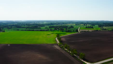 Aerial-view-of-dark-soil-field-and-green-wheat-farmland-with-tree-line,-Latvia