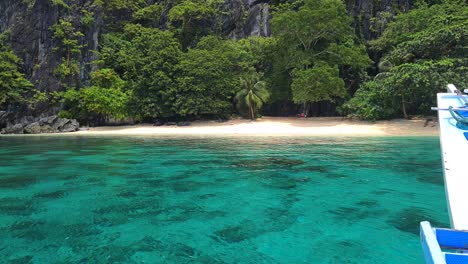 Boat-Arriving-on-Deserted-Tropical-Beach-on-Exotic-Island-Under-Steep-Limestone-Cliffs