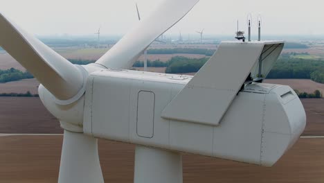 Windkraftanlage-Farm-Nahaufnahme-Der-Gondel-Von-Hinten-Mit-Einer-Drohne-Schwenken-Um-Mit-Ackerland-Im-Hintergrund